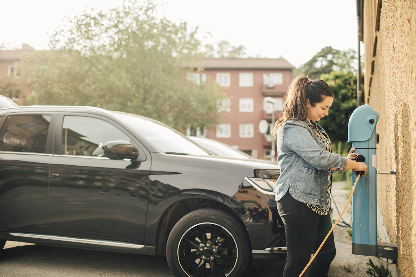 Woman charging electric car outside apartment building