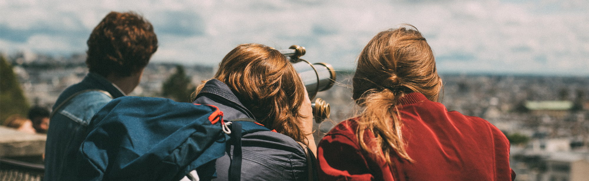 Three young persons looking over a city, one through binoculars