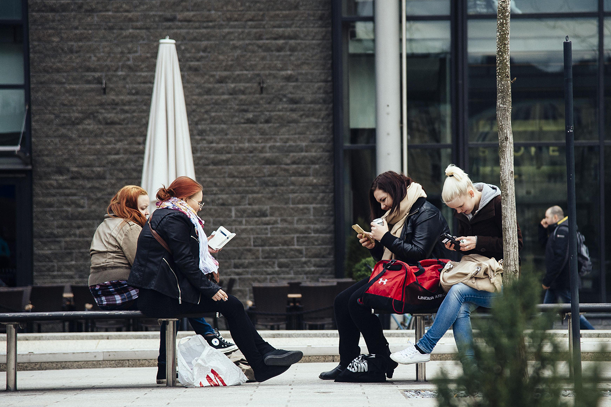 Four young women with phones and books, sitting outside