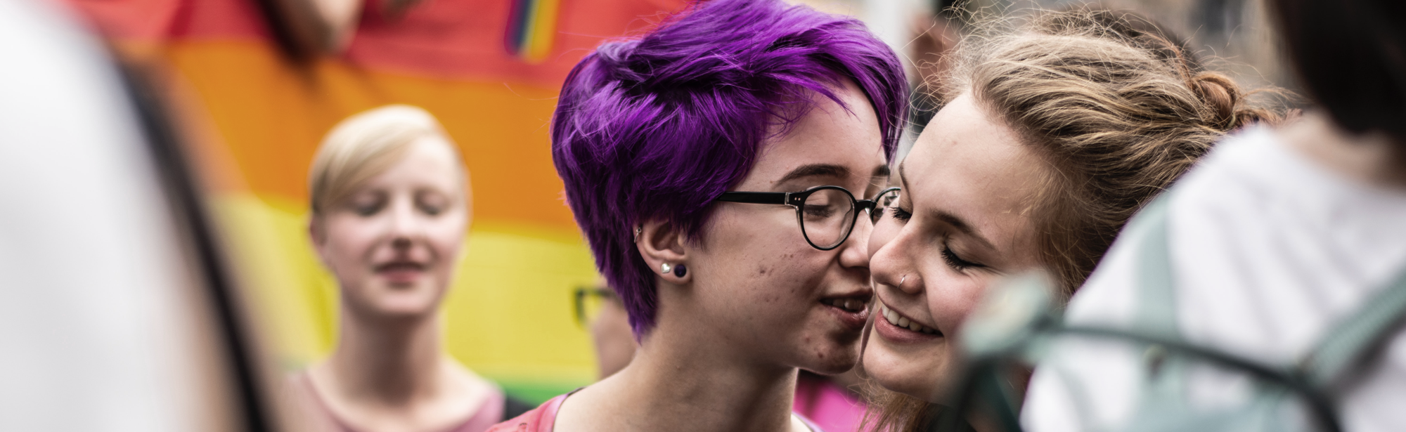 Two persons with rainbow flag in the background