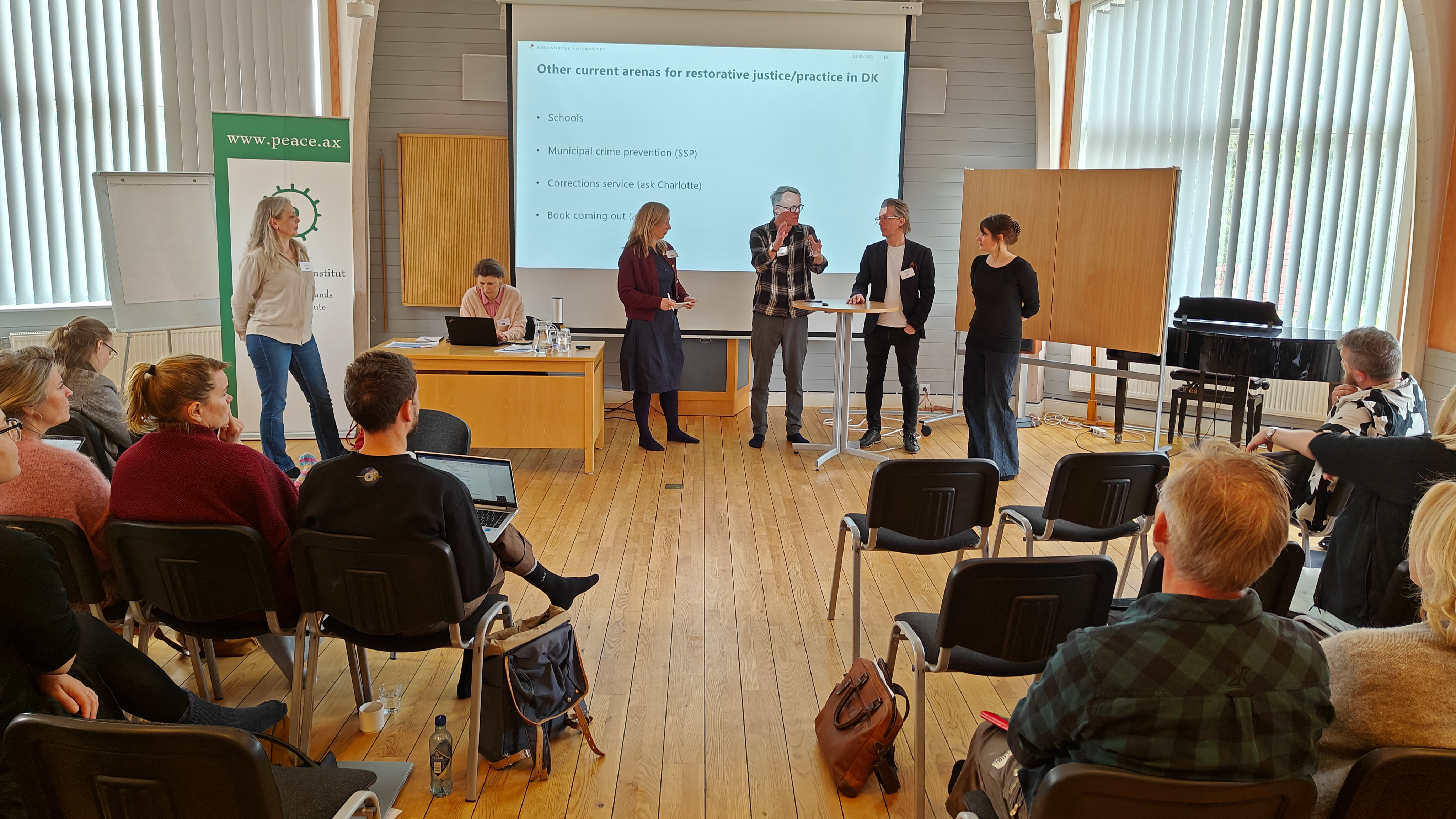 The picture is showing a room with four people standing in front of an audience. 