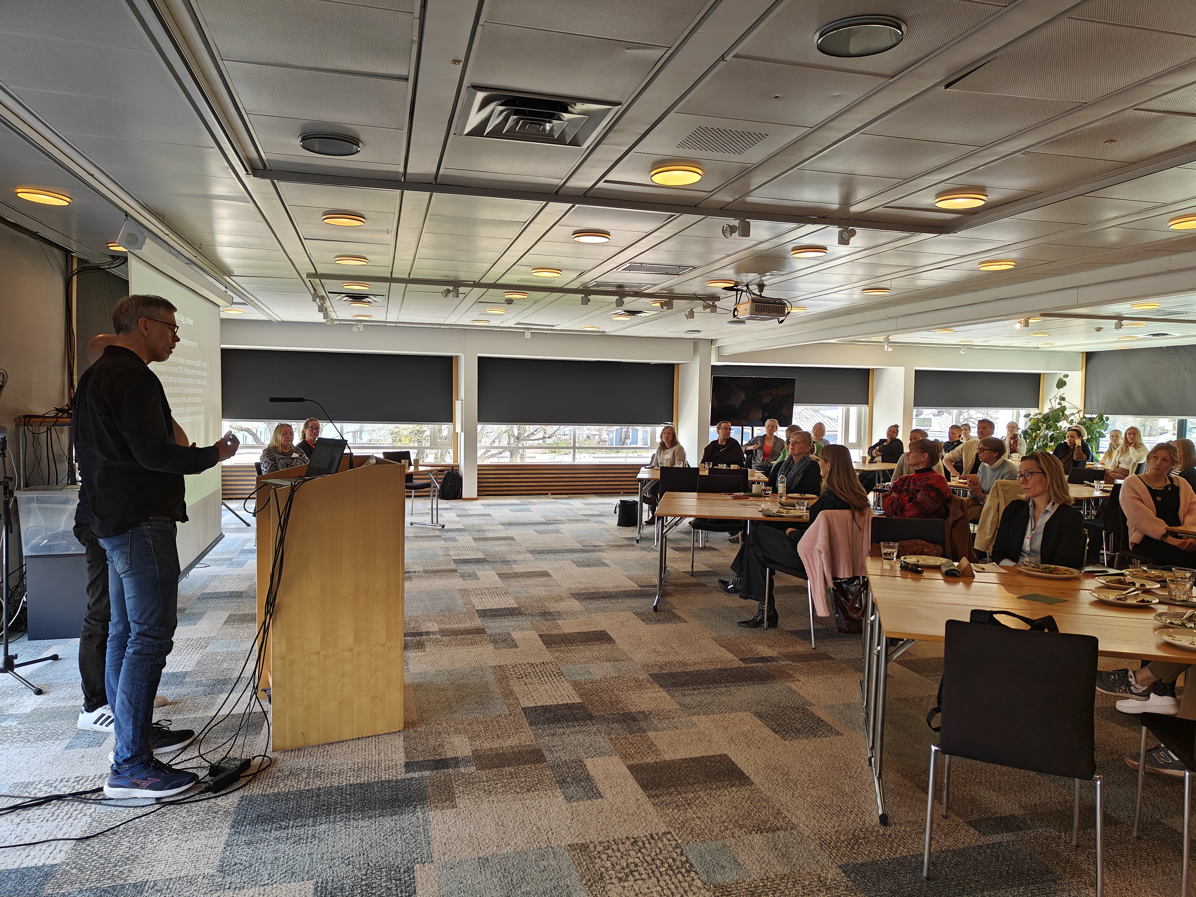 The picture is showing a room with two people standing in front of an audience. 