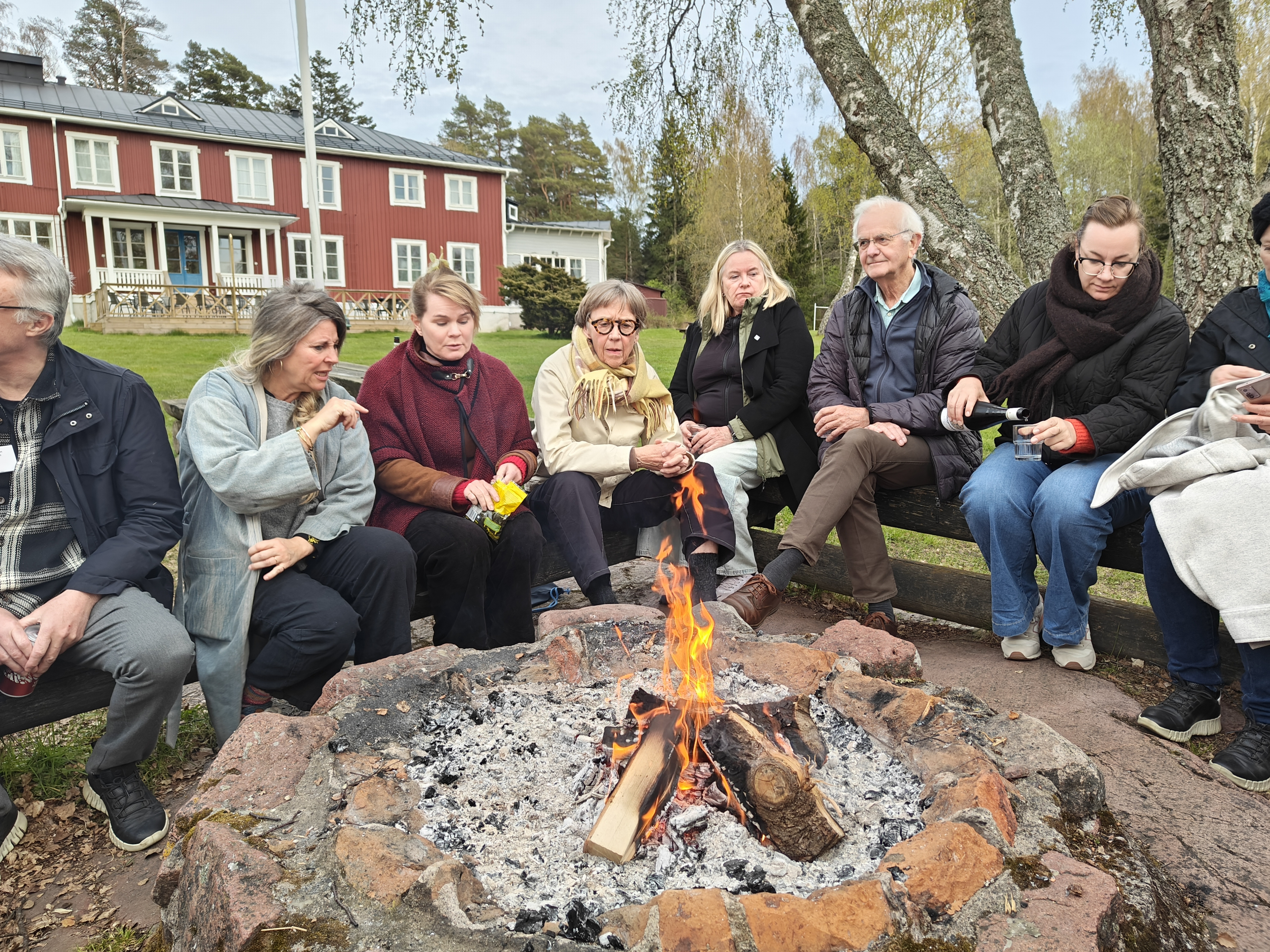 The picture is showing eight people sitting around a fire outside.