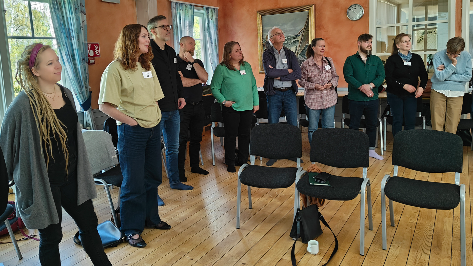 The picture is showing a room of people standing in a half-circle. 